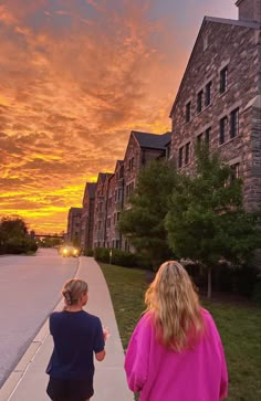 two girls walking down the sidewalk in front of an old brick building at sunset or dawn