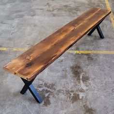 a wooden bench sitting on top of a cement floor next to a yellow line in a parking lot