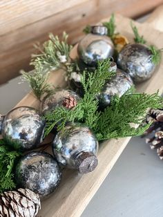 some silver balls and pine cones are on a wooden board with greenery in the middle