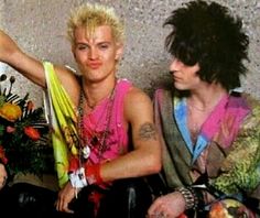 two young men sitting next to each other in front of a wall with flowers on it