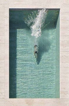 an aerial view of a person swimming in a pool with blue water and white walls