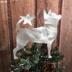 a white dog ornament sitting on top of a christmas tree next to pine cones