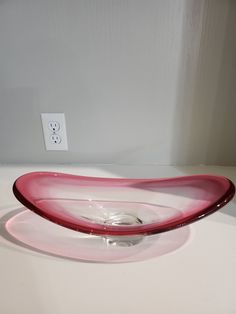 a red glass bowl sitting on top of a white counter next to a light switch