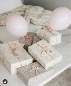 several wrapped presents and balloons on a table with a white bed in the back ground