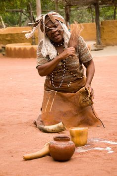 a woman in native clothing is making something out of clay and other items on the ground