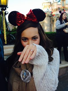 a woman wearing minnie mouse ears and holding her hand up to her face while standing in front of a castle