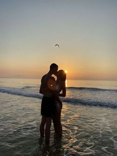 a couple kissing in the ocean at sunset