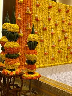 an arrangement of flowers on display in front of a wall with yellow and orange decorations