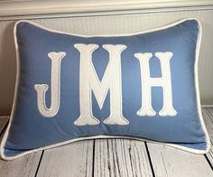 a blue and white pillow with the letter j on it's side, sitting on a wooden floor