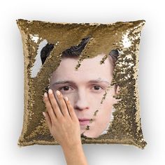 a woman holding her hand up to a sequin pillow with the face of a young man on it