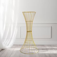 a gold wire vase sitting on top of a wooden floor next to a white wall