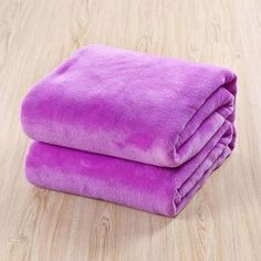 two purple towels folded on top of each other in front of a wooden table with wood flooring