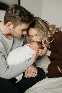 a man and woman holding a baby in their arms while sitting on a bed together