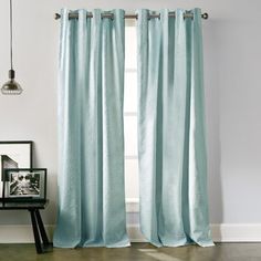 a living room with a window covered in light blue drapes and a black end table