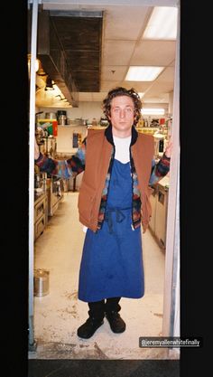 a woman standing in a kitchen wearing an apron and jacket with her arms out to the side