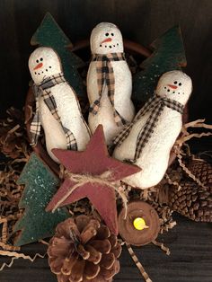 three snowmen sitting in a basket with pine cones