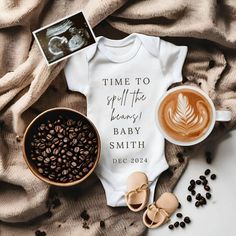 a baby's bodysuit and some coffee are on the bed next to it