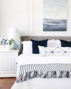 a white bed with blue and white pillows on top of it next to a painting