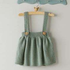 a baby's green dress hanging on a wall next to a wooden hanger