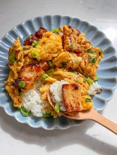 a blue plate topped with rice and chicken next to a wooden spoon on top of a table