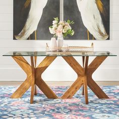 a glass table with two birds painted on the wall behind it and flowers in vases