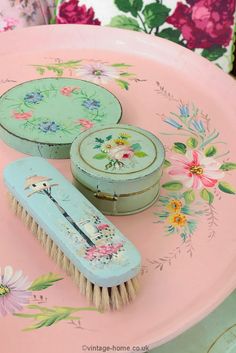 three tins and a brush sitting on top of a pink table with floral designs