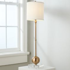 a lamp that is on top of a table next to a window with a white curtain