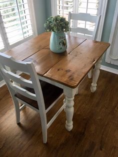 a wooden table with two white chairs and a blue vase on top of the table