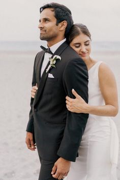 a man and woman standing next to each other in front of the ocean on their wedding day