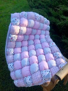 a pink and white baby blanket sitting on top of a wooden bench in the grass