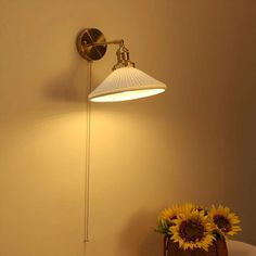 a lamp that is on the wall next to a vase with sunflowers in it