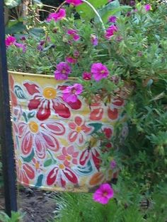 a painted flower pot sitting in the middle of a garden filled with purple and red flowers