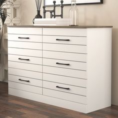 a white dresser with black handles next to a mirror and plant in vases on the wall