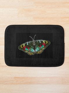 a colorful butterfly sitting on top of a black bath mat next to a wooden floor