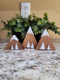 three wooden mountains with trees on them sitting next to a potted plant in front of a wall