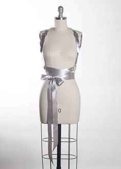 Romantic & light, the Twilight Harness is a softer take on the leather harness. The leather contrasts beautifully with the metal hardware and the soft satin ribbons which wrap around the waist to tie into a bow. Extra-soft and silky double-faced satin ribbon imported from Japan gives this piece a luxurious look and feel.Fit is adjustable with buckles and straps. Silver toned nickel plated steel hardware. Shown in silver metallic leather (silver leather is now lined and stitched). Also available Book Harness, Gown With Belt, Vegan Books, Romantic Lighting, Bow Belt, Satin Ribbons, Leather Harness, Fashion Catalogue, Black Gown