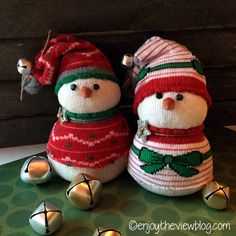 two knitted snowmen sitting next to each other with bells around their necks and wearing hats