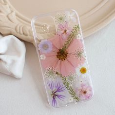 an iphone case with flowers on it sitting next to a white plate and napkins