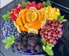 a platter filled with fruits and vegetables on top of a stove burner topped with oranges, raspberries, lemons, blueberries