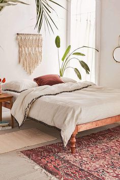 a bedroom with a bed, rug and plants in the corner on either side of the window