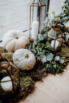 some white pumpkins and greenery are on the ground next to two small lanterns