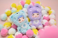 two small stuffed animals sitting next to each other on top of some colorful pom poms