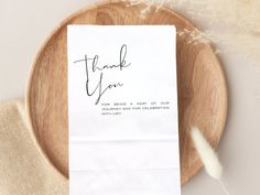 a thank you note sitting on top of a wooden plate next to a white feather