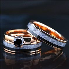 two wedding rings with black diamonds on them sitting next to each other in front of a dark background