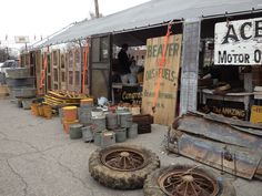 several old tires and other items are on the ground in front of a building that is being used as a flea market