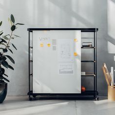 a white board with yellow stickers on it next to a potted plant and other office supplies