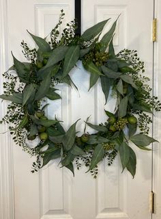 a wreath with green leaves and berries hanging on the front door to greet someone's home