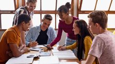 a group of people sitting around a table with notebooks and papers in front of them