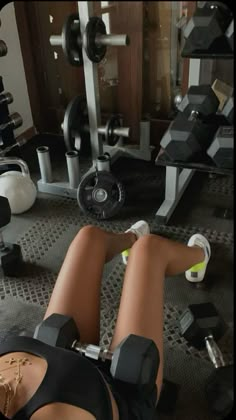 a woman laying on the ground in front of a gym machine with dumbbells