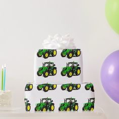 a birthday cake with tractor wrapping on it and balloons in the background, along with two candles